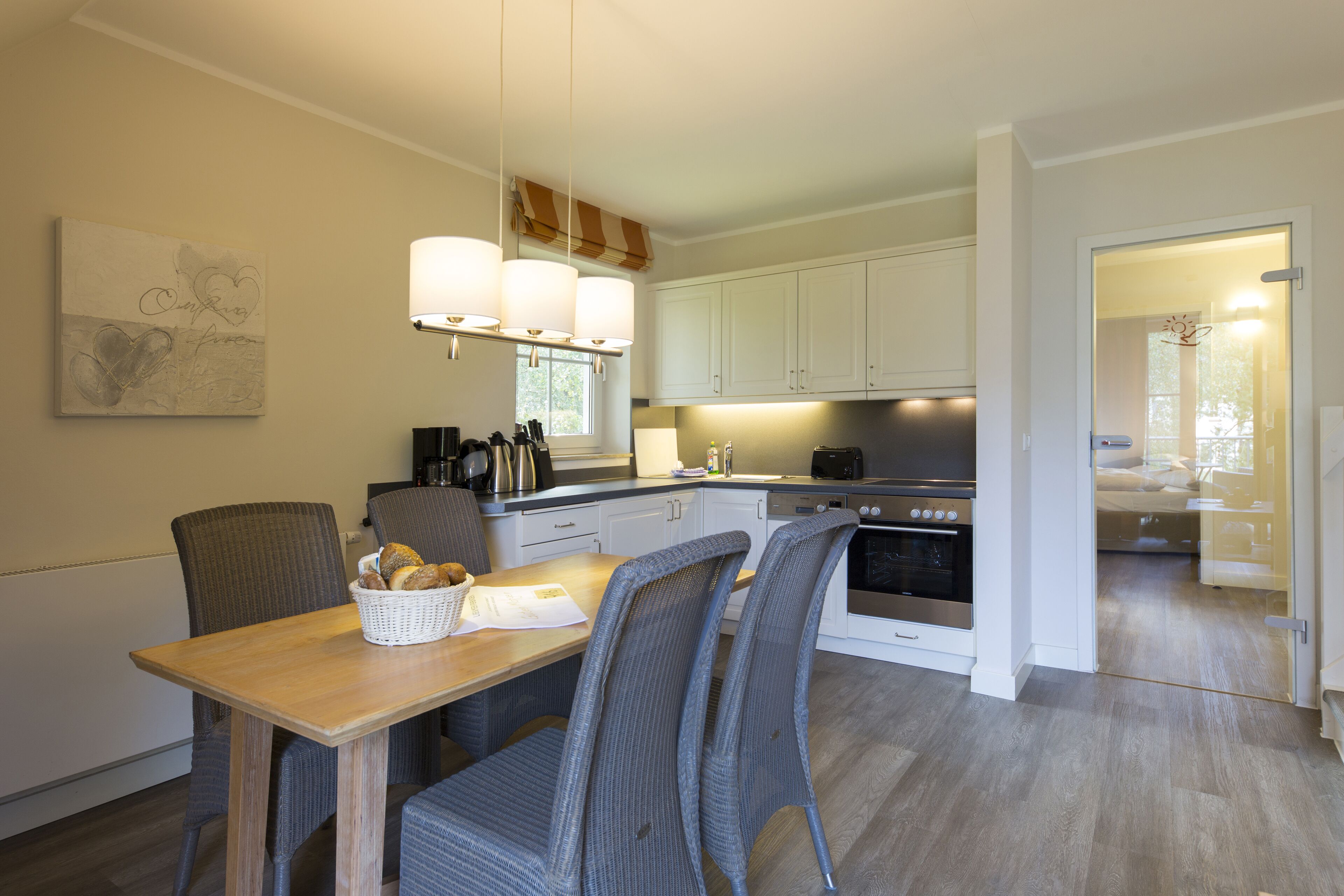 A modern kitchen with white cabinets, a dining table with chairs, and a basket of bread on the table.