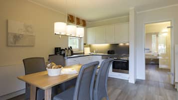 A modern kitchen with white cabinets, a dining table with chairs, and a basket of bread on the table.
