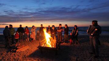 Un grupo de personas reunidas alrededor de una fogata en la playa al atardecer.