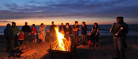A group of people gathered around a campfire on a beach at sunset.