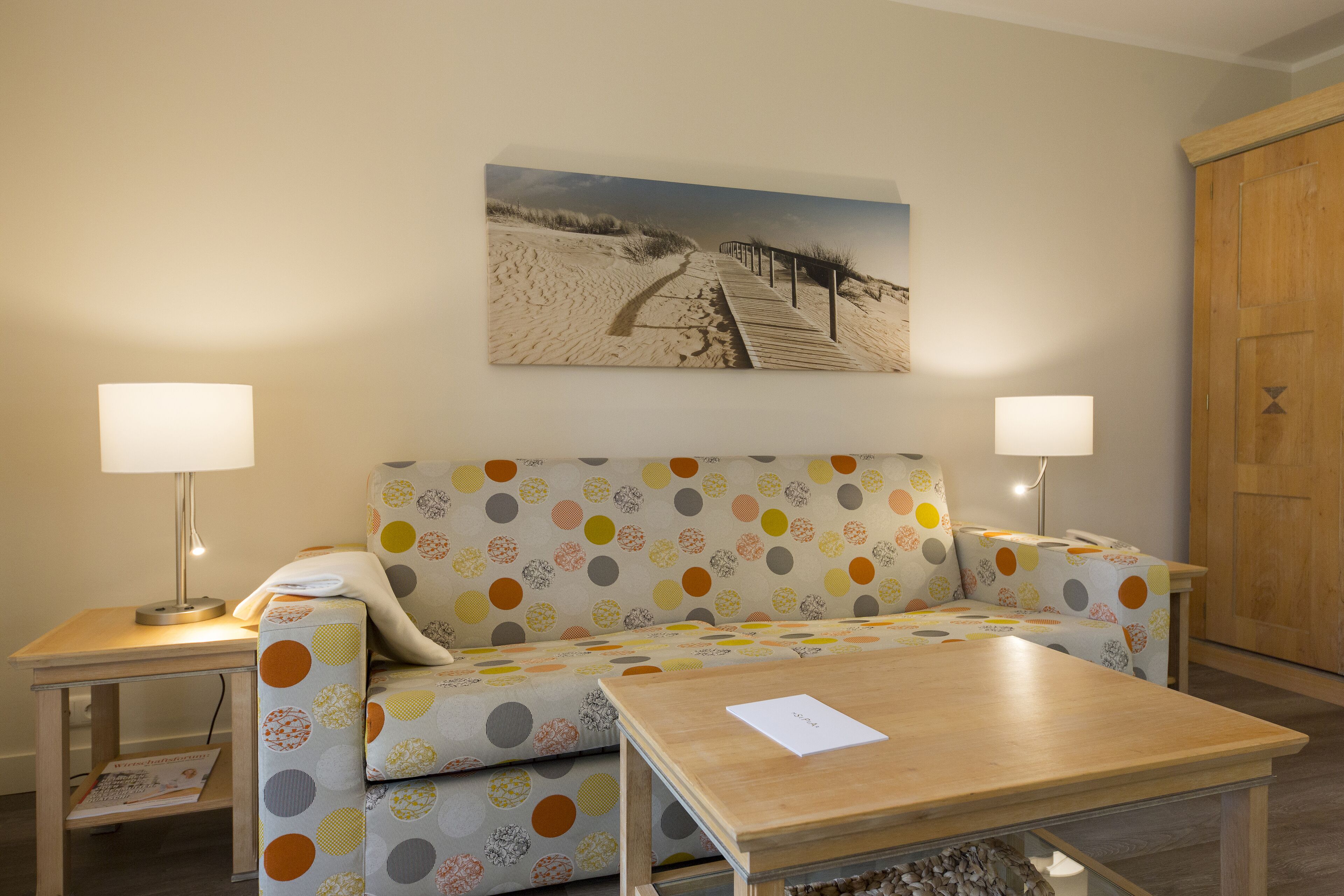 A room with a patterned sofa, a wooden coffee table, and a painting of a beach scene.