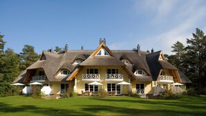 Ein großes, zweistöckiges Haus mit einem Strohdach, mehreren Balkonen und einem gepflegten Rasen.