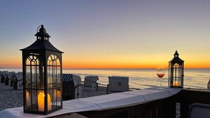 Blick auf einen Strand mit Strandkörben, einer Holzterrasse und einem Glas Rotwein.
