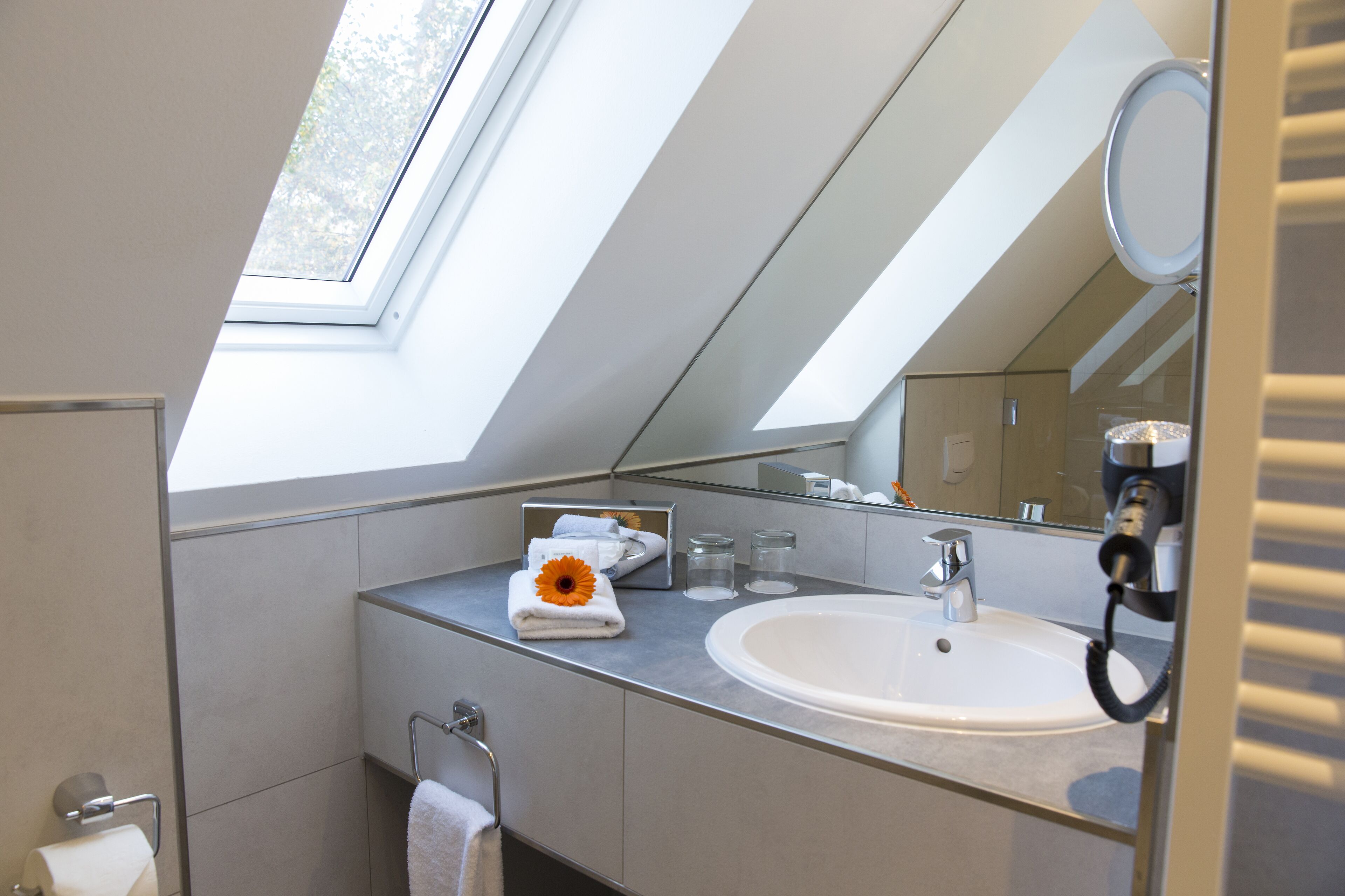 Une salle de bain moderne dotée d’une lucarne, d’un grand miroir et d’un lavabo.