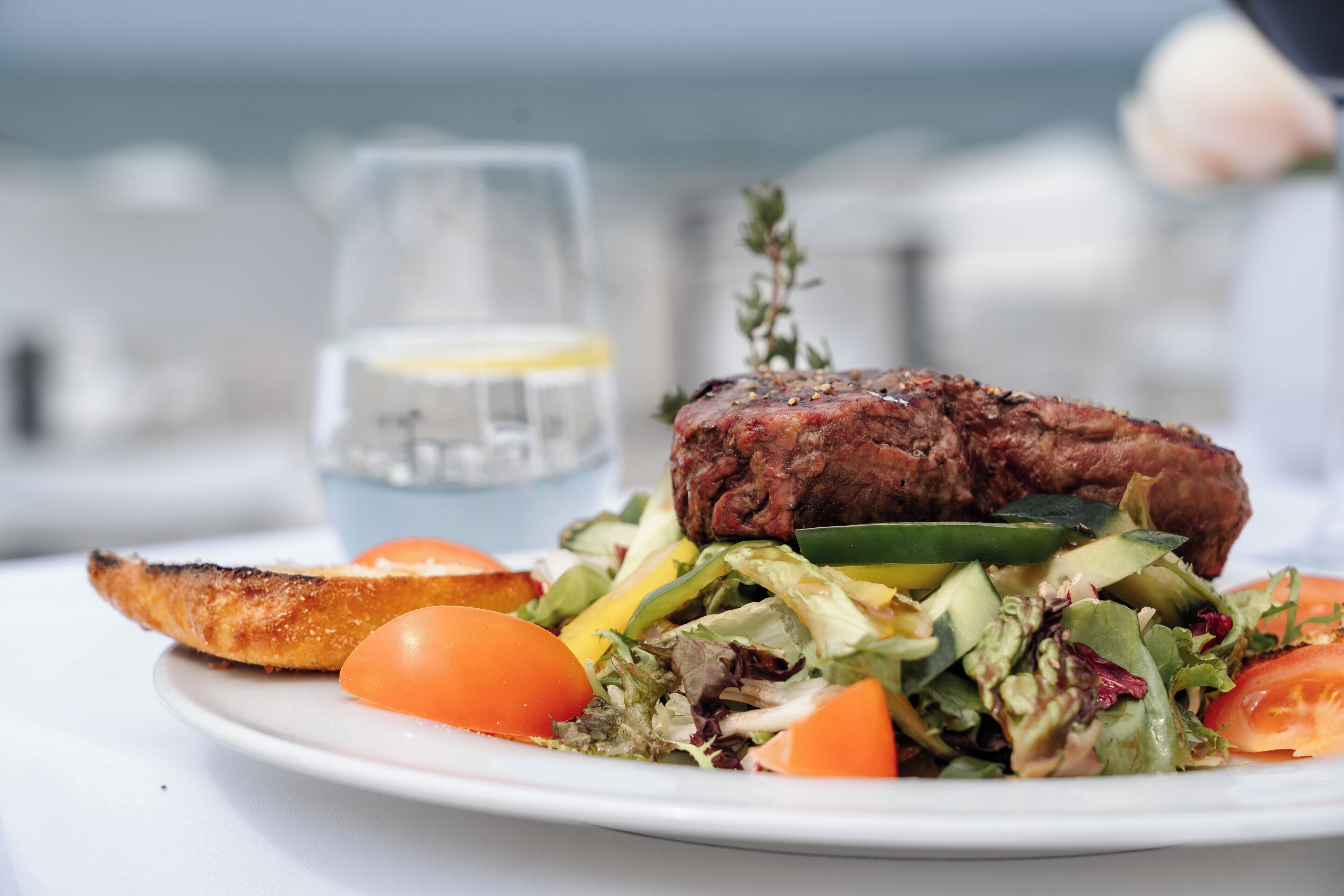A plate with a steak, vegetables, and a glass of water.