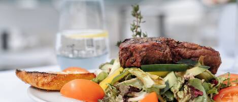 A plate with a steak, vegetables, and a glass of water.