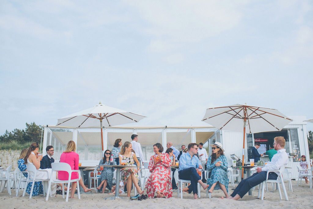 Un área de estar al aire libre con sillas blancas y sombrillas, rodeada por una estructura blanca, probablemente un restaurante o bar frente al mar.