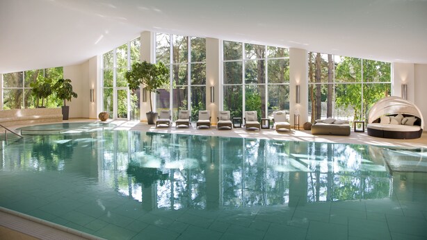 Ein Innenpool mit klaren Glaswänden, Liegestühlen und einer Sonnenliege.