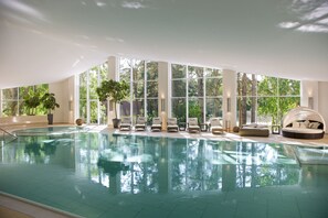 An indoor swimming pool with clear glass walls, lounge chairs, and a sun lounger. - Ferienwohnungen Fischland (Ostseebad Dierhagen)