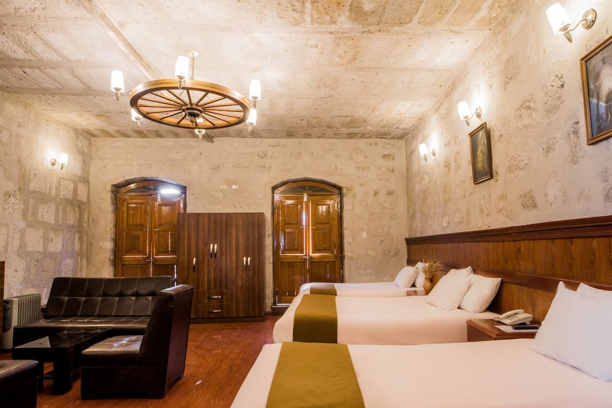 Habitación de hotel con dos camas, un sofá de cuero, un armario de madera y un candelabro.
