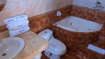 Un baño con lavamanos, inodoro y bañera. Hay toallas apiladas en el lavamanos.
