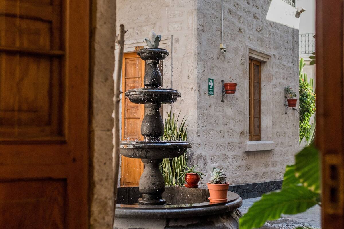 Un patio con una fuente de piedra, plantas en macetas y una puerta de madera.
