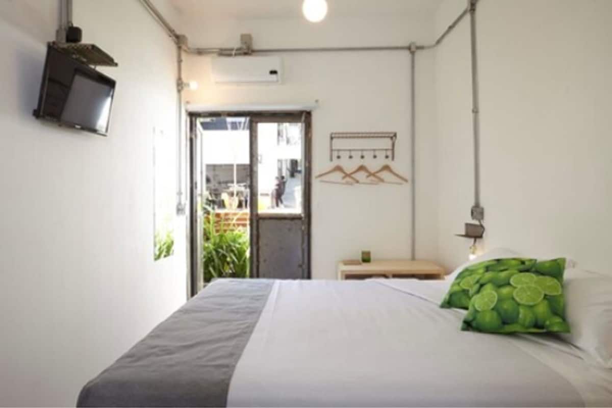 A bedroom with a bed, a TV mounted on the wall, a door leading outside, and a wall-mounted light fixture.