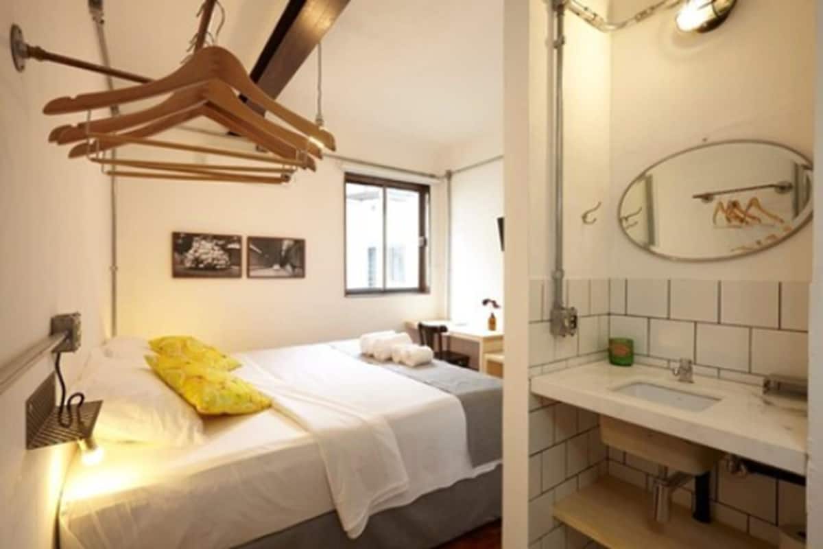 A hotel room with a bed, a bedside table, a mirror, and a hanging clothes rack.