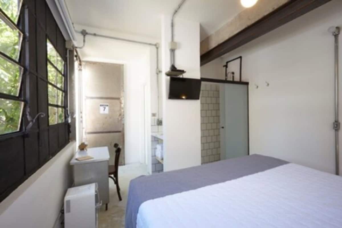 A bedroom with a bed, a small desk, a chair, and a window.