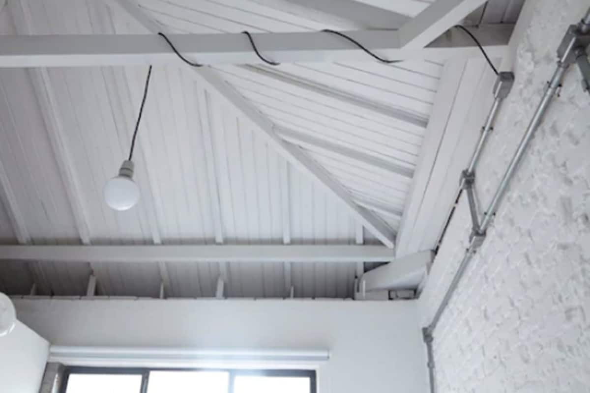 A room with a high ceiling, exposed beams, and a white brick wall.