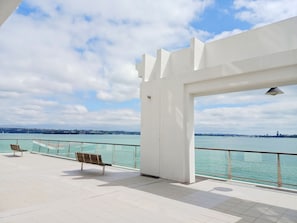 A balcony with a view of the sea and a distant city skyline.