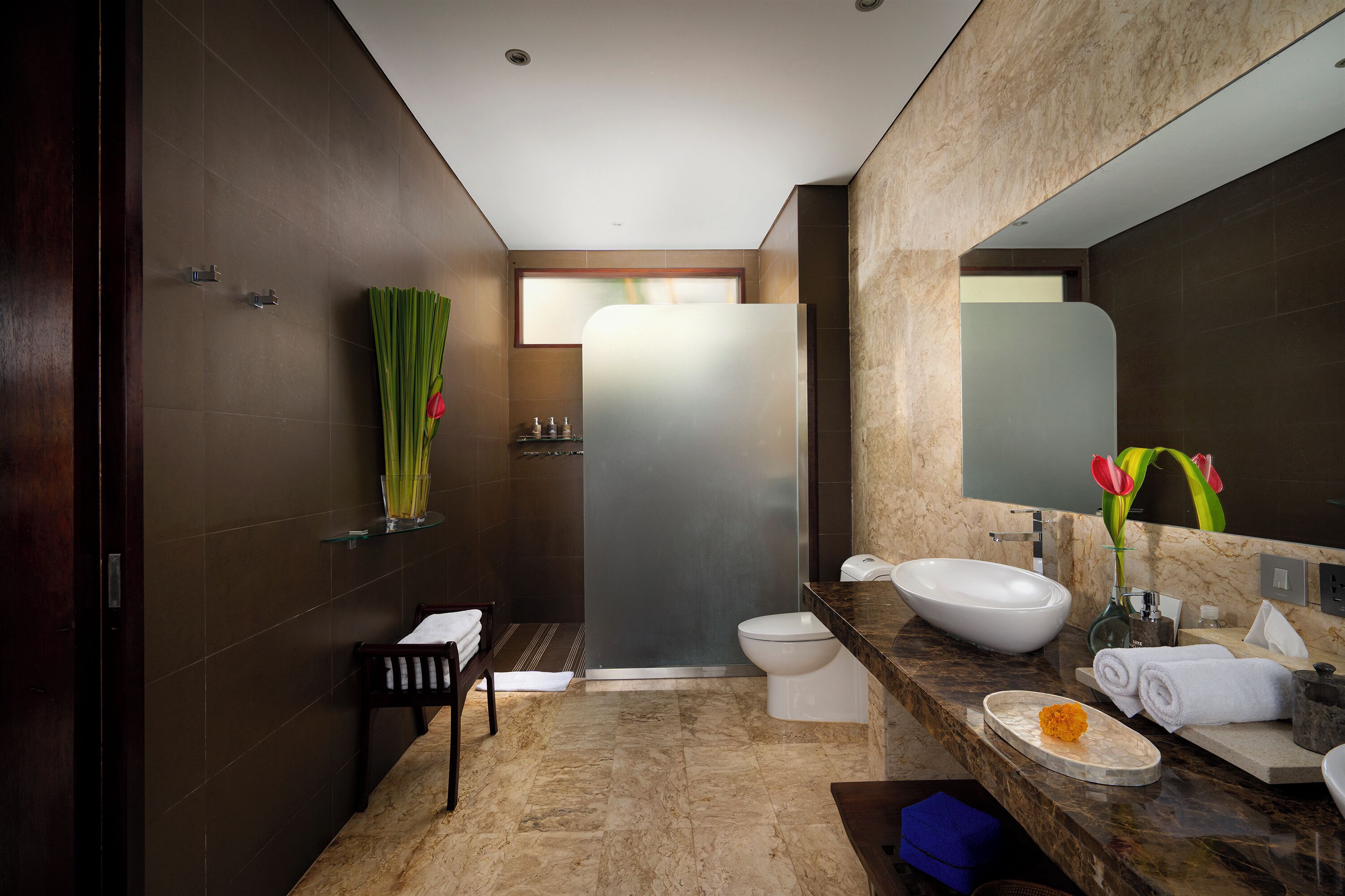 A modern bathroom with a large mirror, a sink, and a toilet. There is a towel rack and a shower area visible.