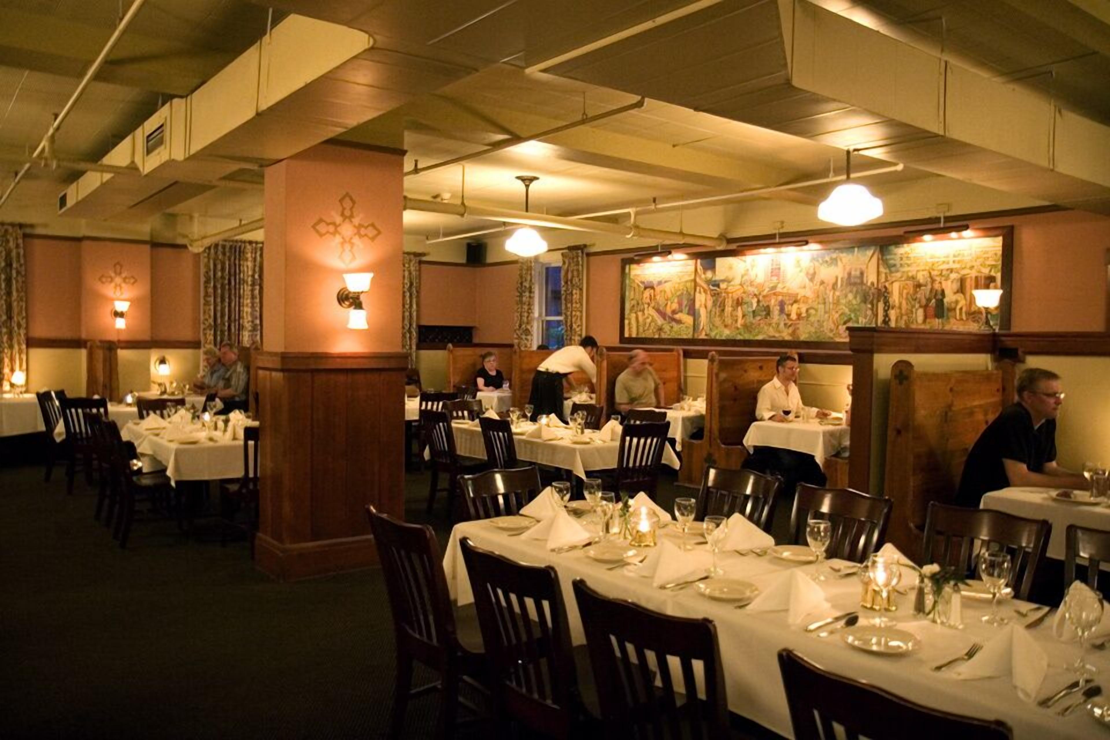 A restaurant with multiple tables set for dining, featuring a classic interior with wooden beams and wall-mounted lighting.