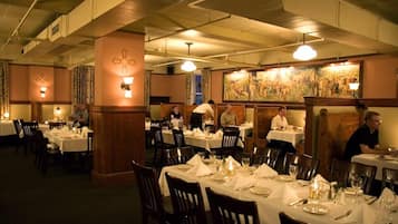 A restaurant with multiple tables set for dining, featuring a classic interior with wooden beams and wall-mounted lighting.