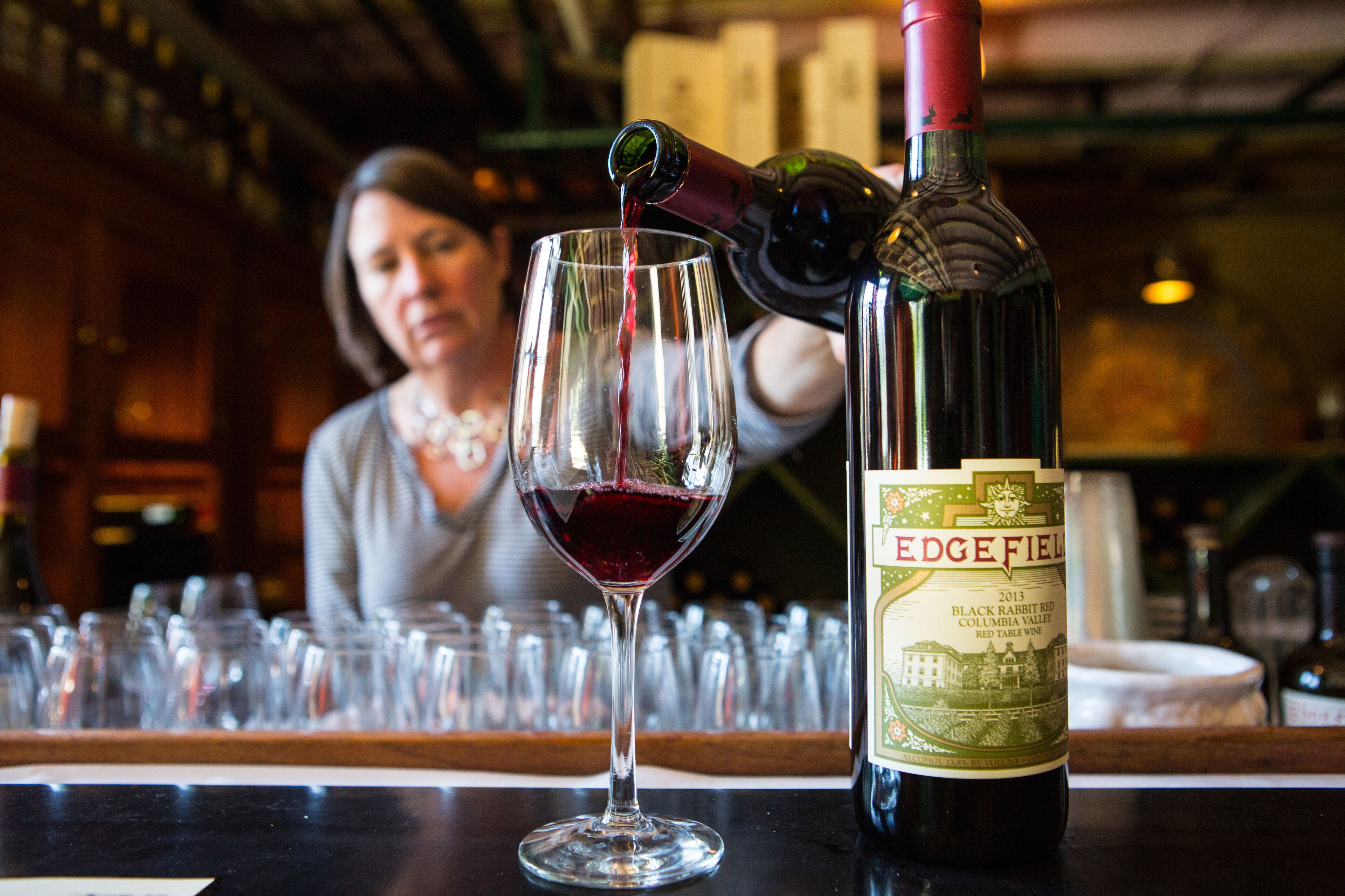 Una botella de vino con la etiqueta "EDGEFIELD" y una copa siendo servida en un bar.