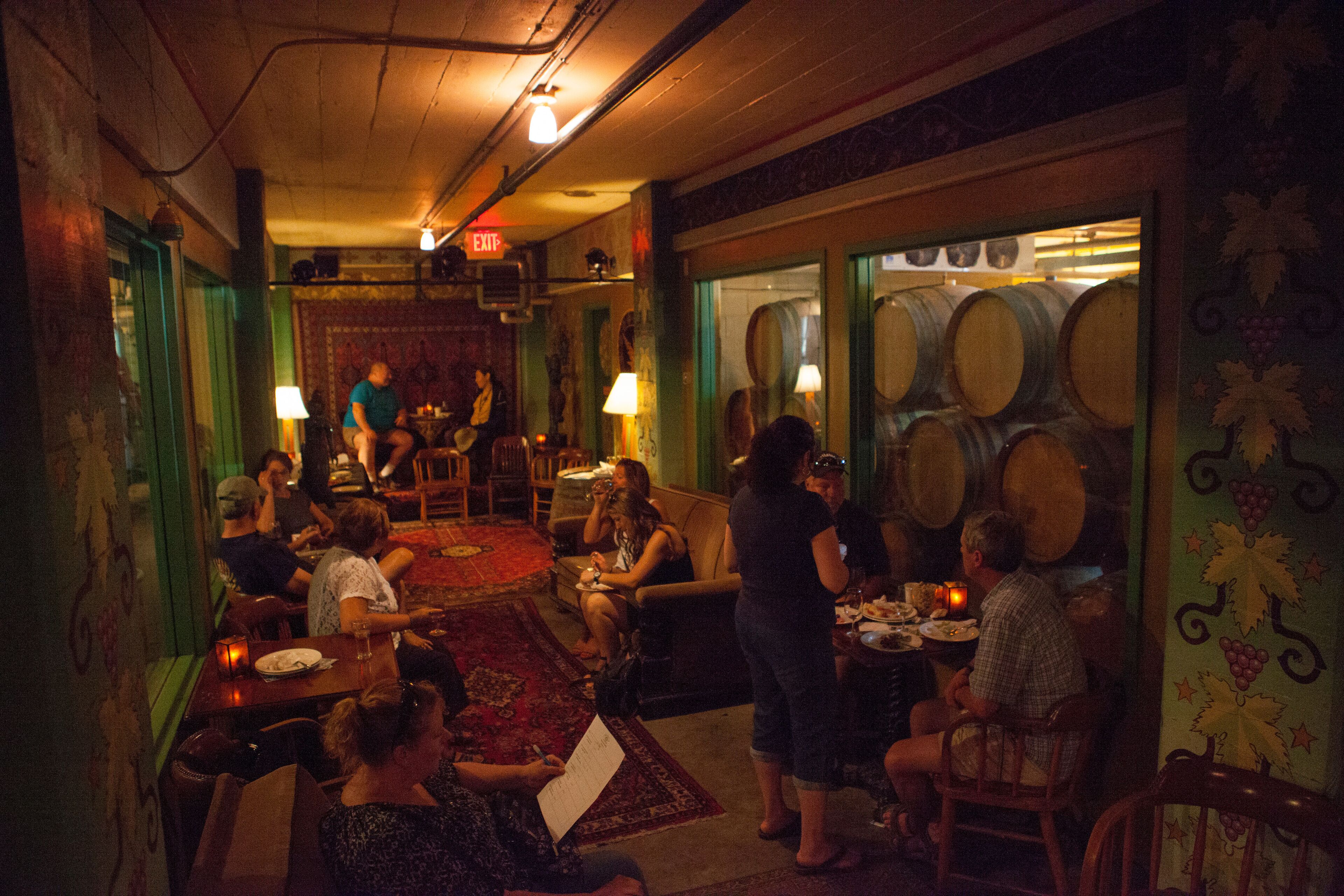 A dimly lit restaurant with patrons seated at tables, a bar area, and a visible exit sign.