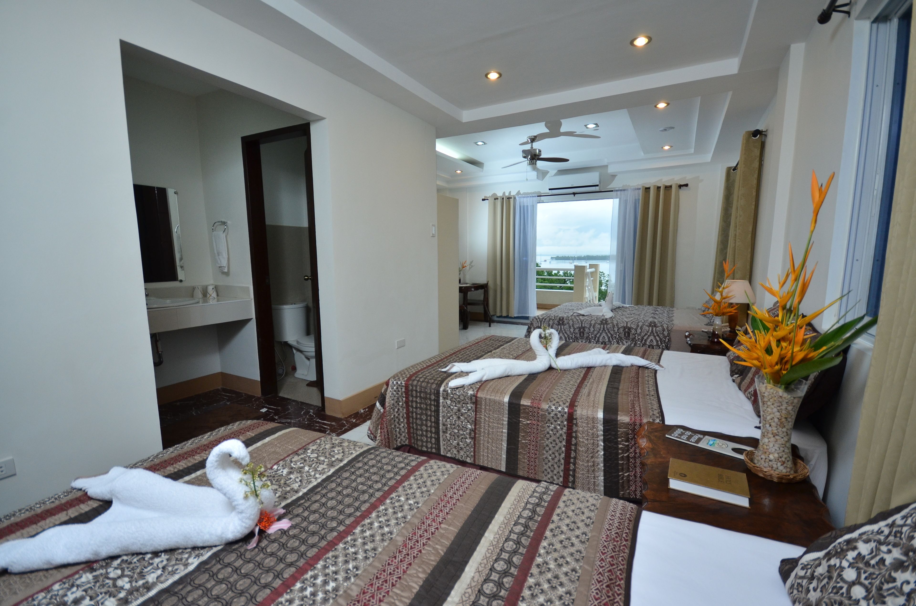 A hotel room with two beds, a ceiling fan, a view of the outdoors, and a vase with flowers on the nightstand.