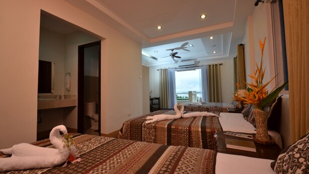 A hotel room with two beds, a ceiling fan, a view of the sea, and a dining area with a table and chairs. - Villa de Sierra Vista (Puerto Princesa)