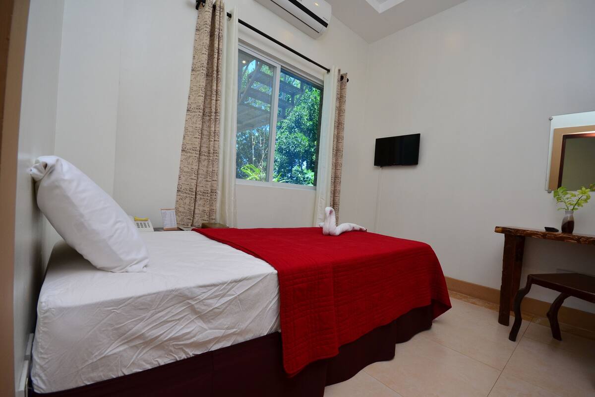 A bed with a white and red bedspread, a white pillow, and a wooden nightstand with a vase of flowers.