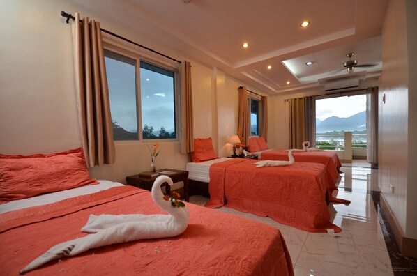 A hotel room with three beds, each with a swan decoration, a large window with curtains, a bedside table with a lamp, and a view of mountains. - Villa de Sierra Vista (Puerto Princesa)