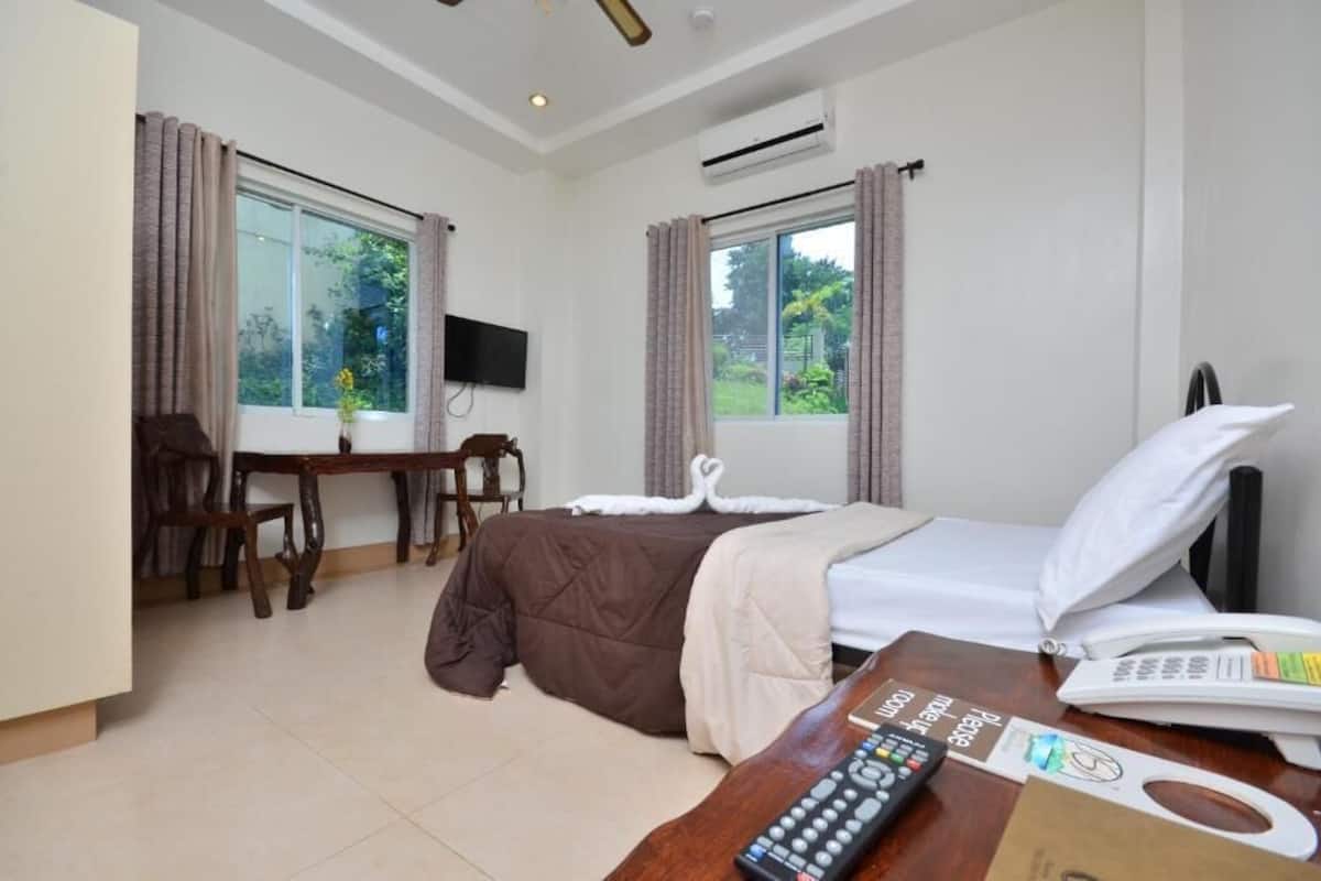 A hotel room with a bed, a desk, a chair, a TV, and a window with curtains.