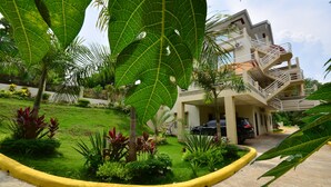 A multi-story building with a parking area and a well-maintained garden with various plants and a yellow curb. - Villa de Sierra Vista (Puerto Princesa)