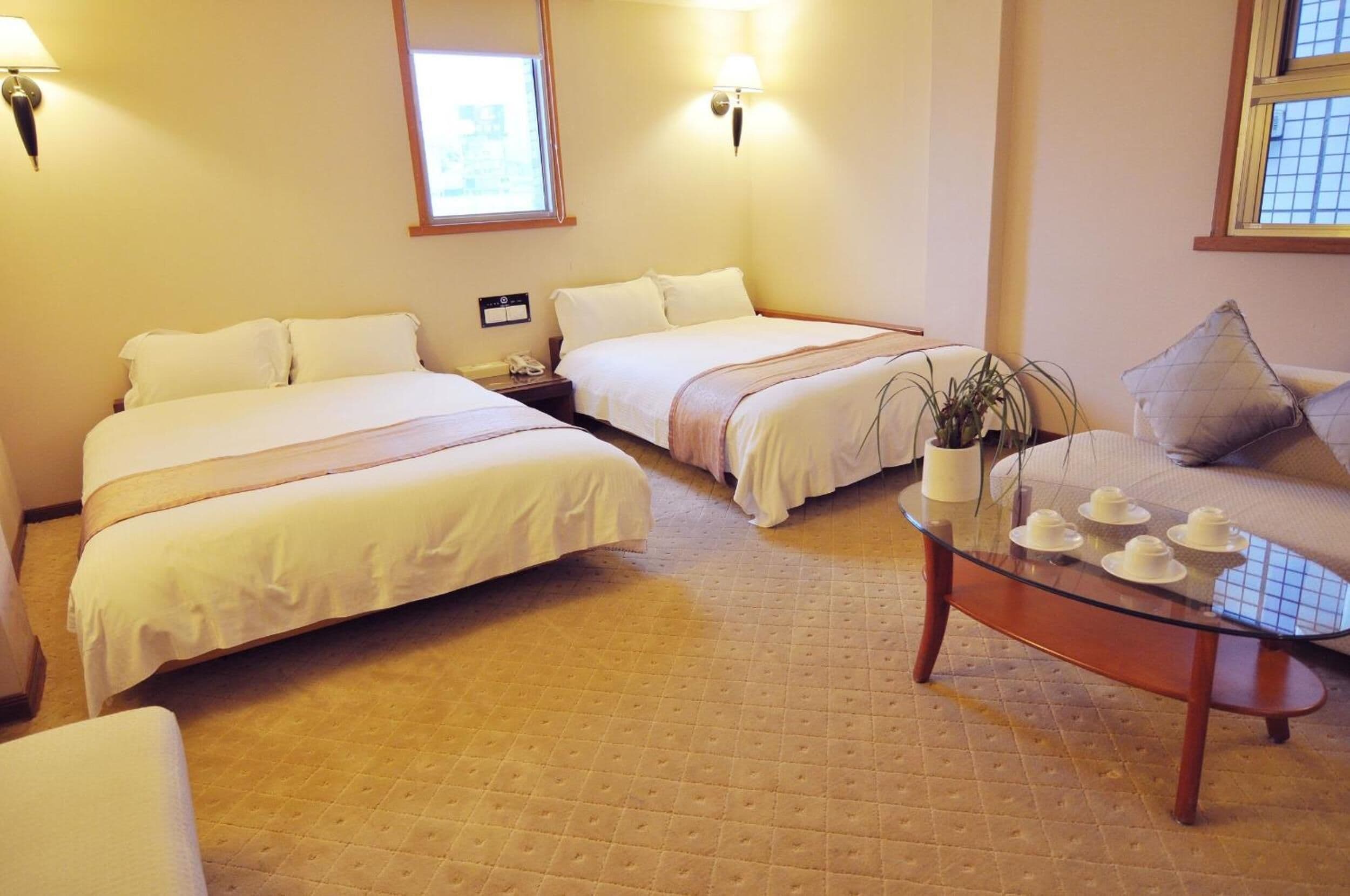 A hotel room with two beds, a glass coffee table, a sofa, and a potted plant.