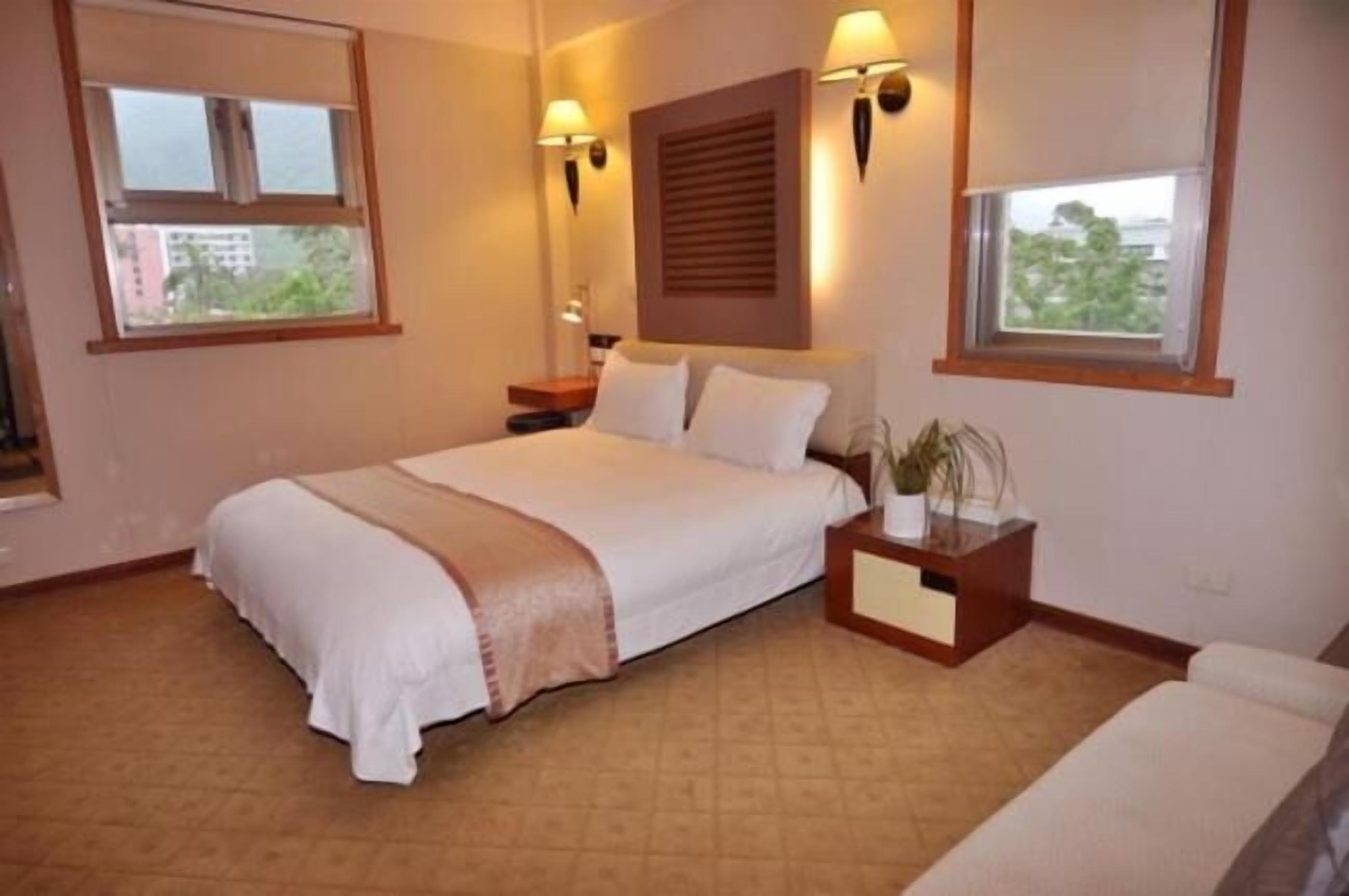 A hotel room with a bed, bedside tables, a nightstand, a window, and a view of the outside.
