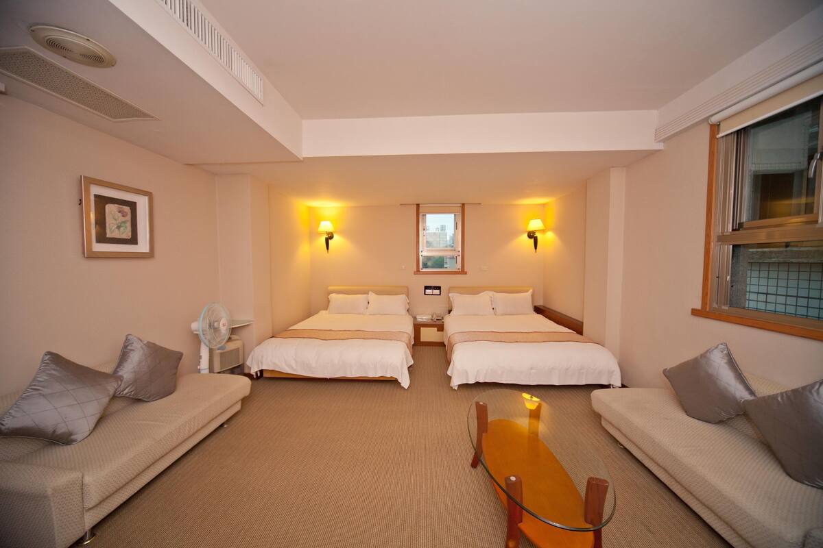 A hotel room with two beds, a sofa, a table, and a window.