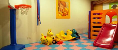 A play area with a basketball hoop, a slide, and colorful toys on a patterned floor.