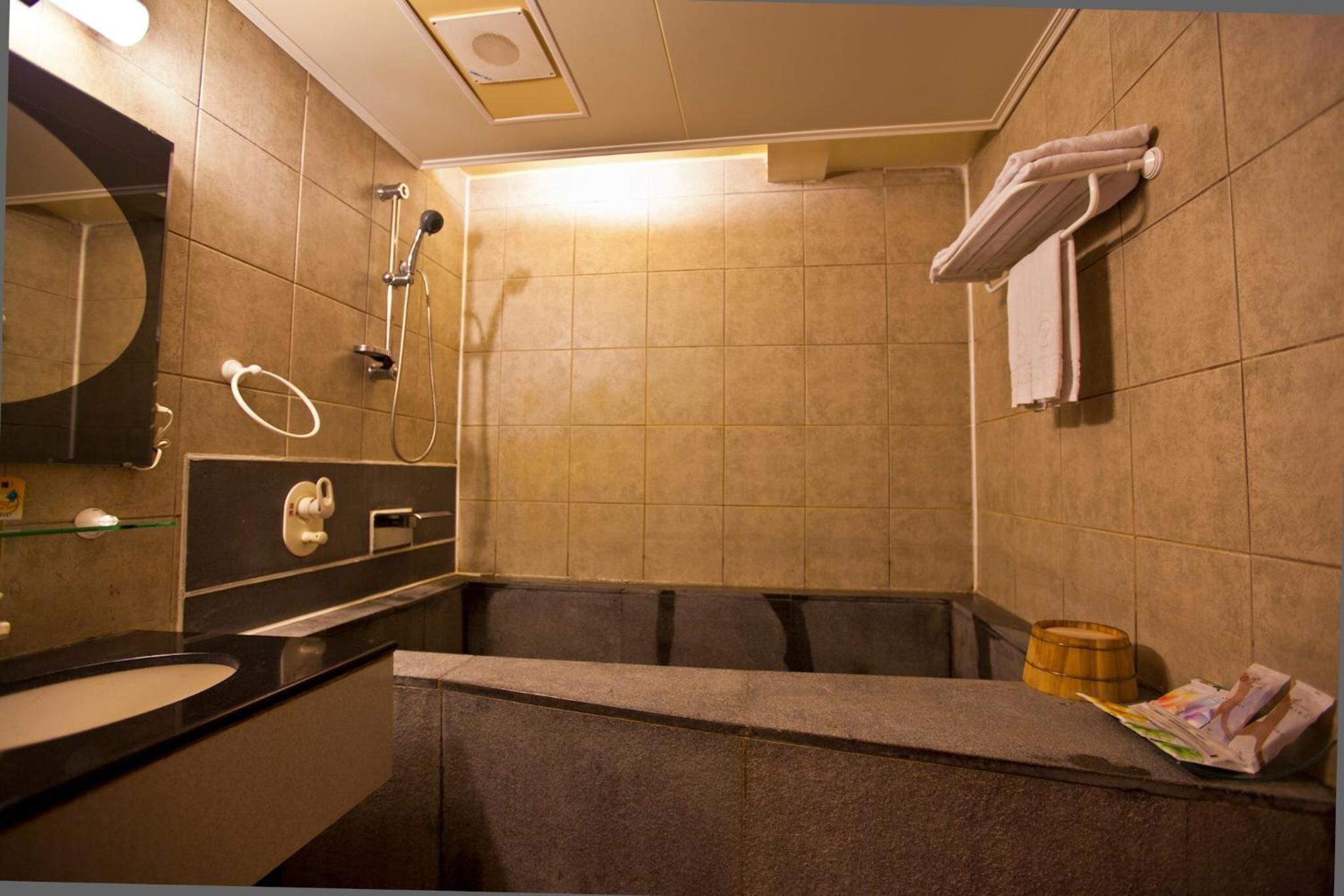 A modern bathroom with a sink, mirror, towel rack, shower, and a wooden bucket.
