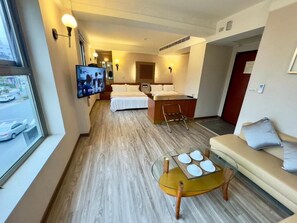 A hotel room with a bed, a sofa, a small table, a TV, and a window with a view of the street. - Tian Long Hotel (Jiaoxi)