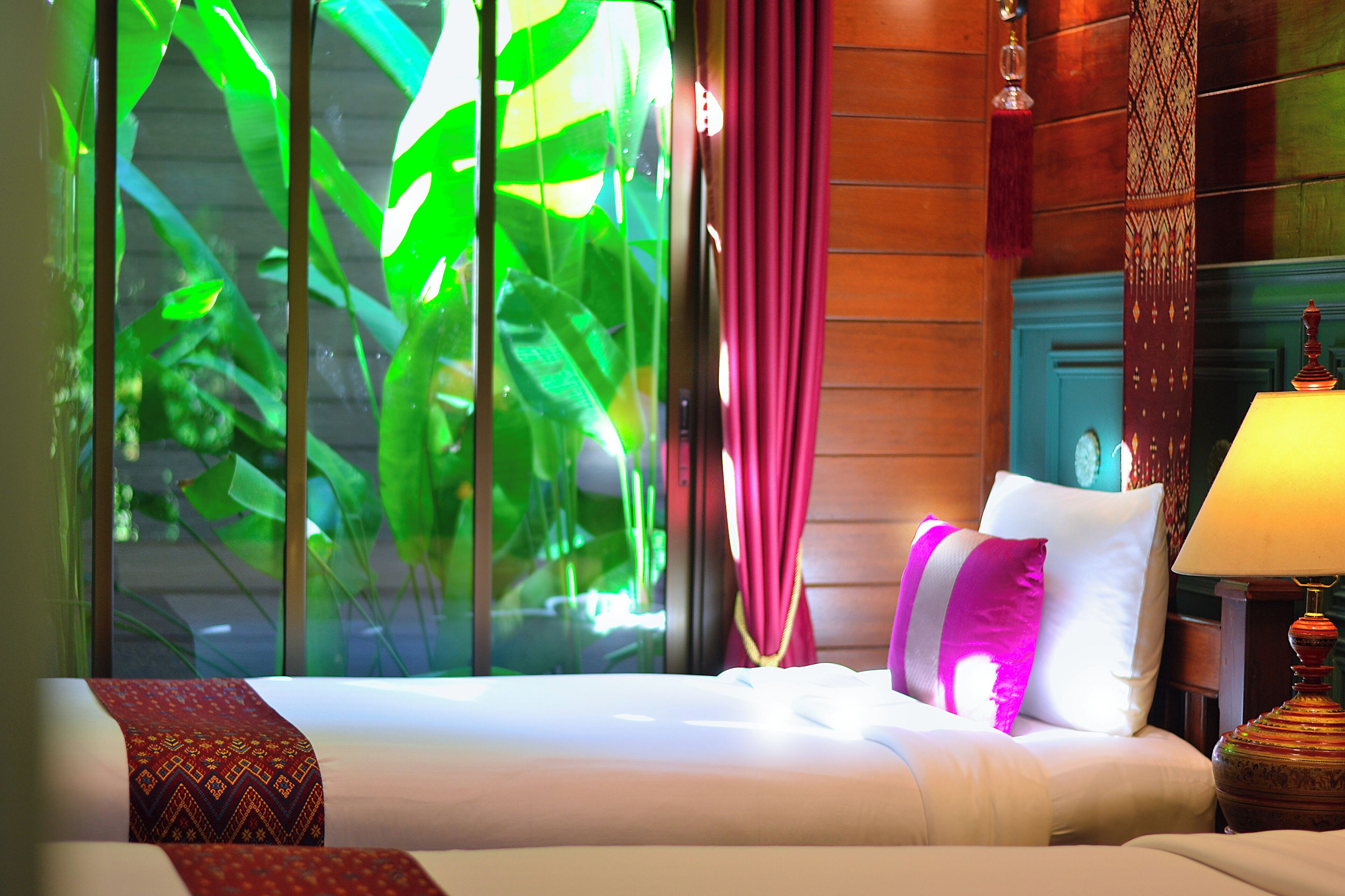 Een hotelkamer met een bed, een lamp, een raam met gordijnen en uitzicht op groen buiten.