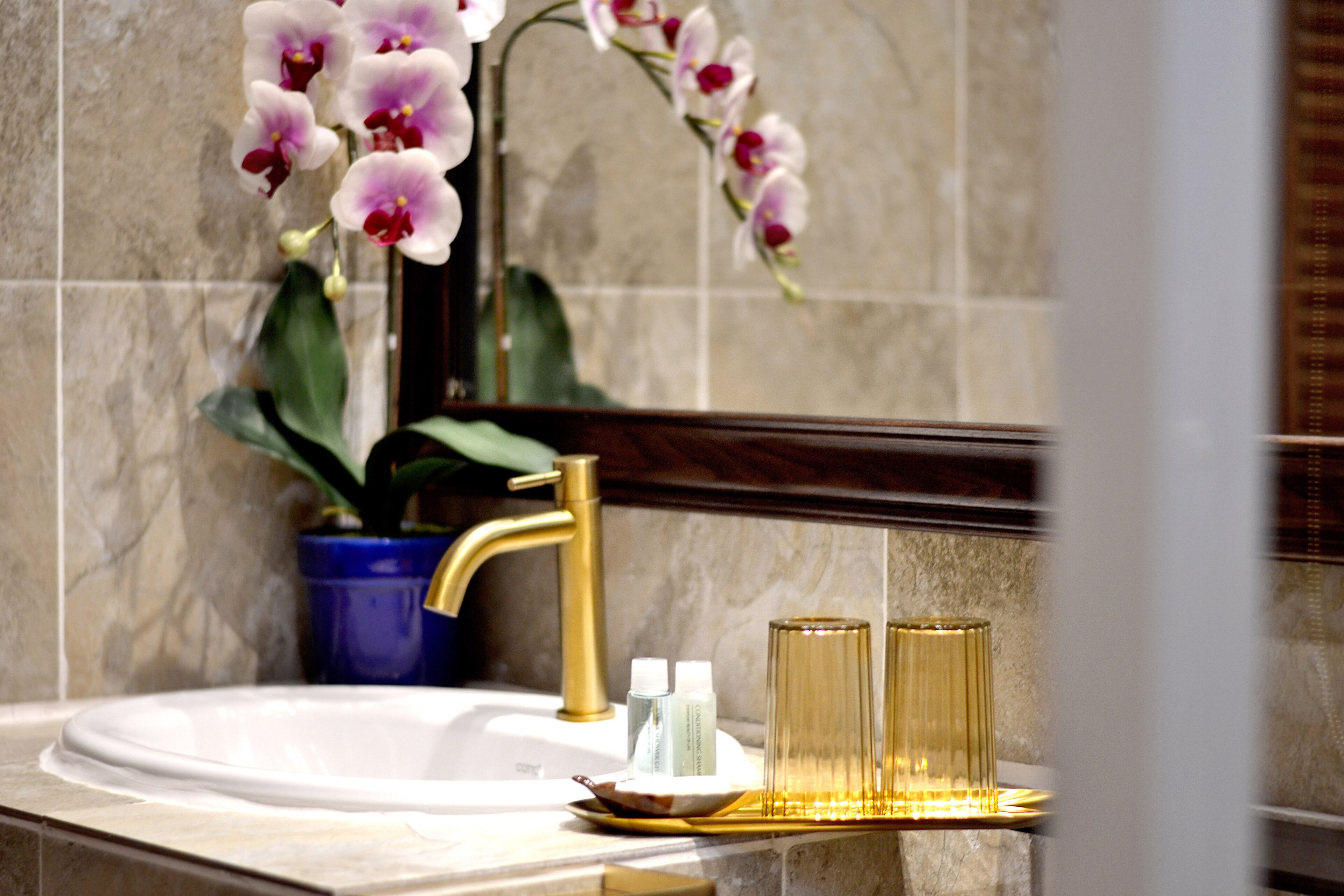 Un baño con lavamanos blanco, grifo dorado y una orquídea en maceta.