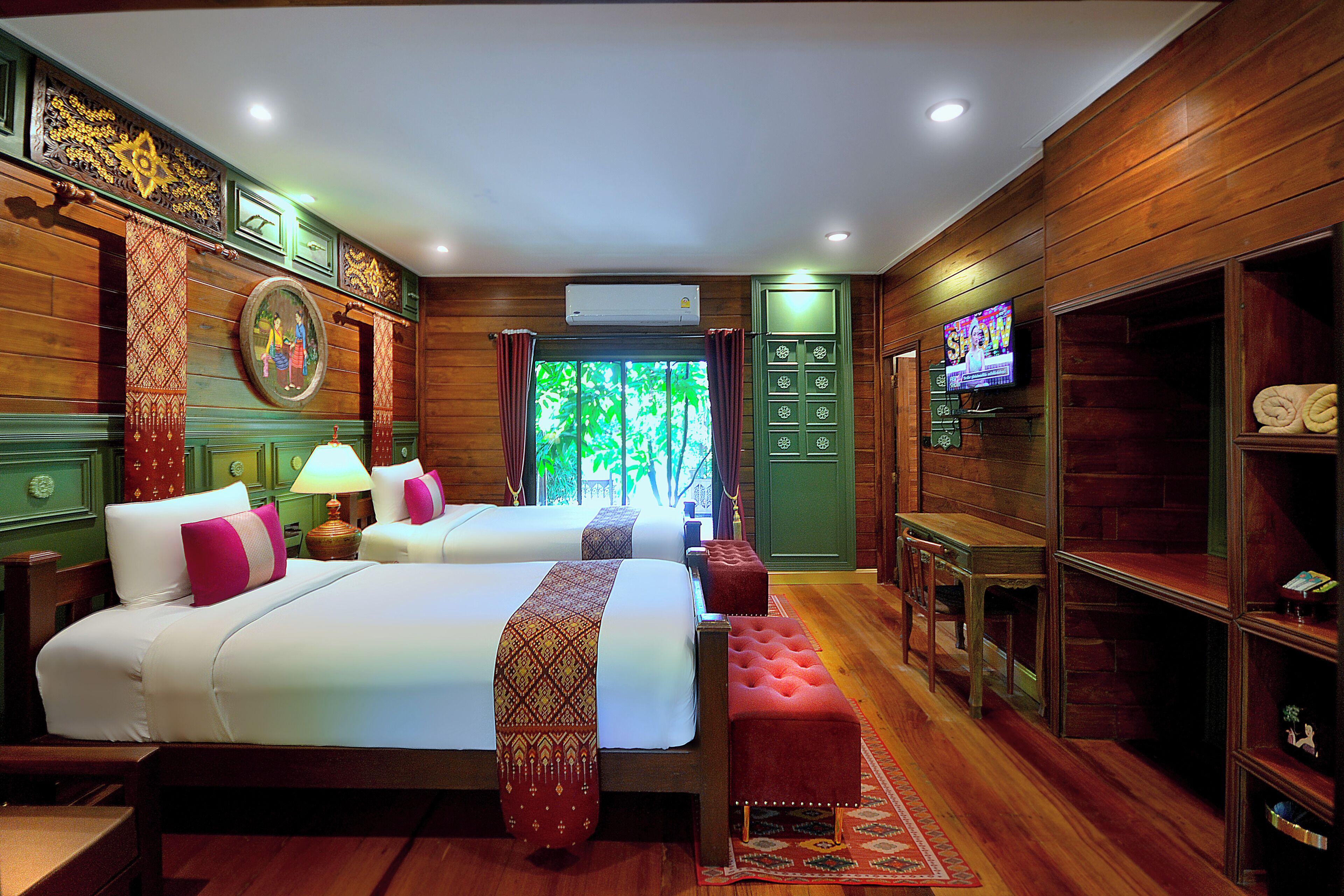 A hotel room with two beds, a television, wooden paneling, and a view of greenery.