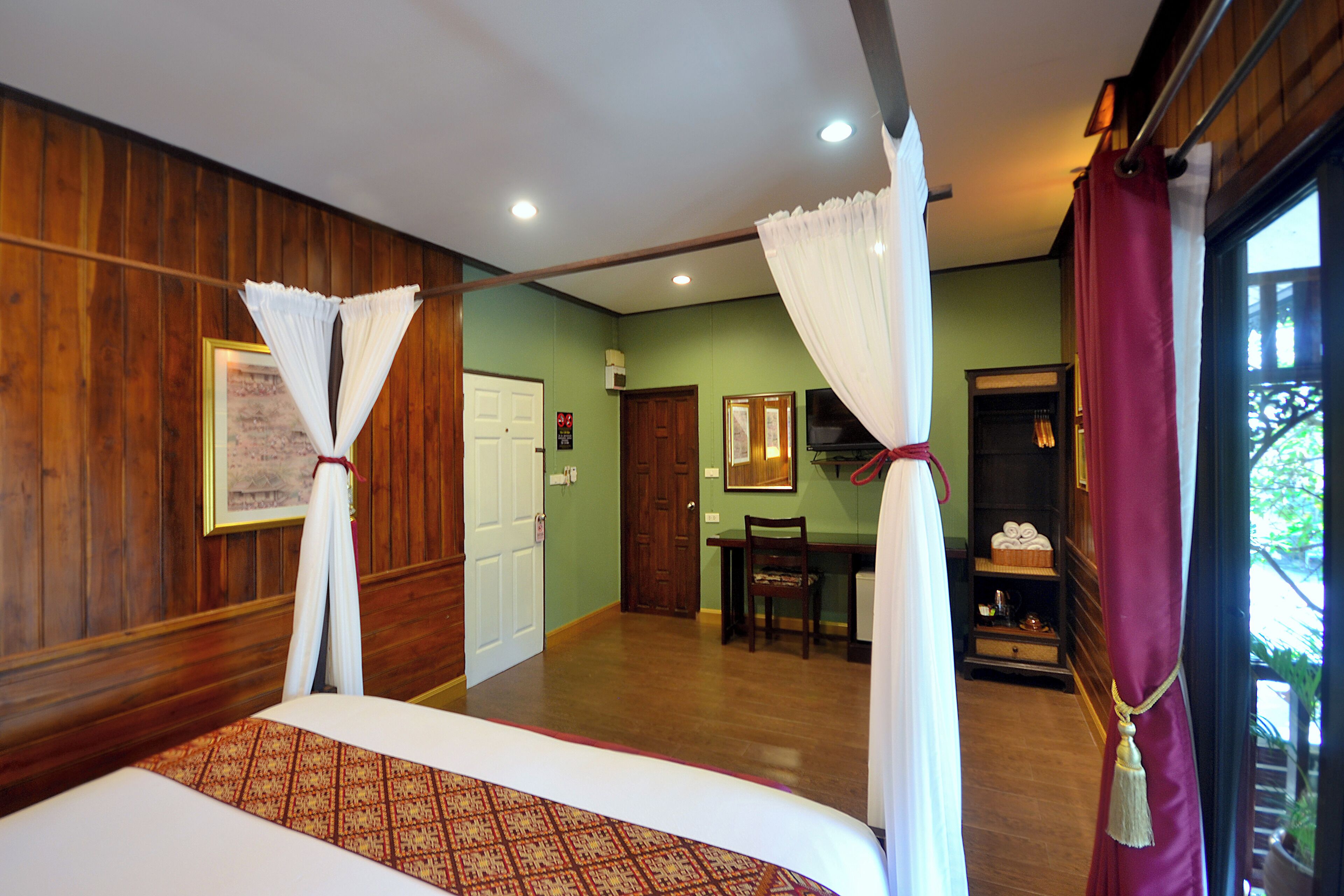A room with a bed, a desk, and a chair. There is a door and a window with curtains.