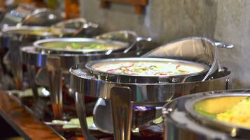 Una barra de buffet con diversos platos en recipientes metálicos.