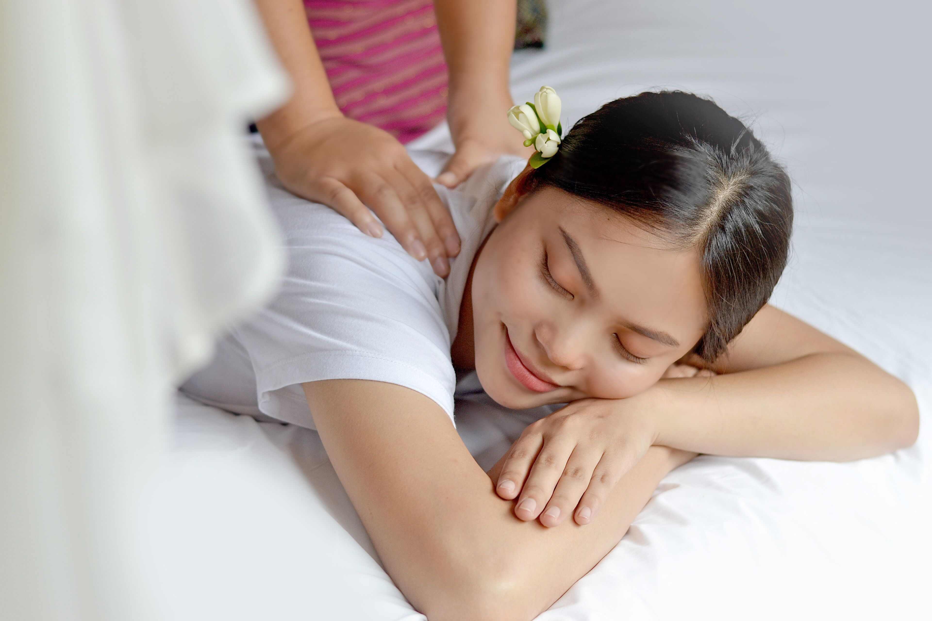 A person lying on a bed with a pillow, another person is giving a massage.