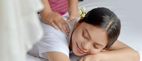 A person lying on a bed with a pillow, another person is giving a massage.