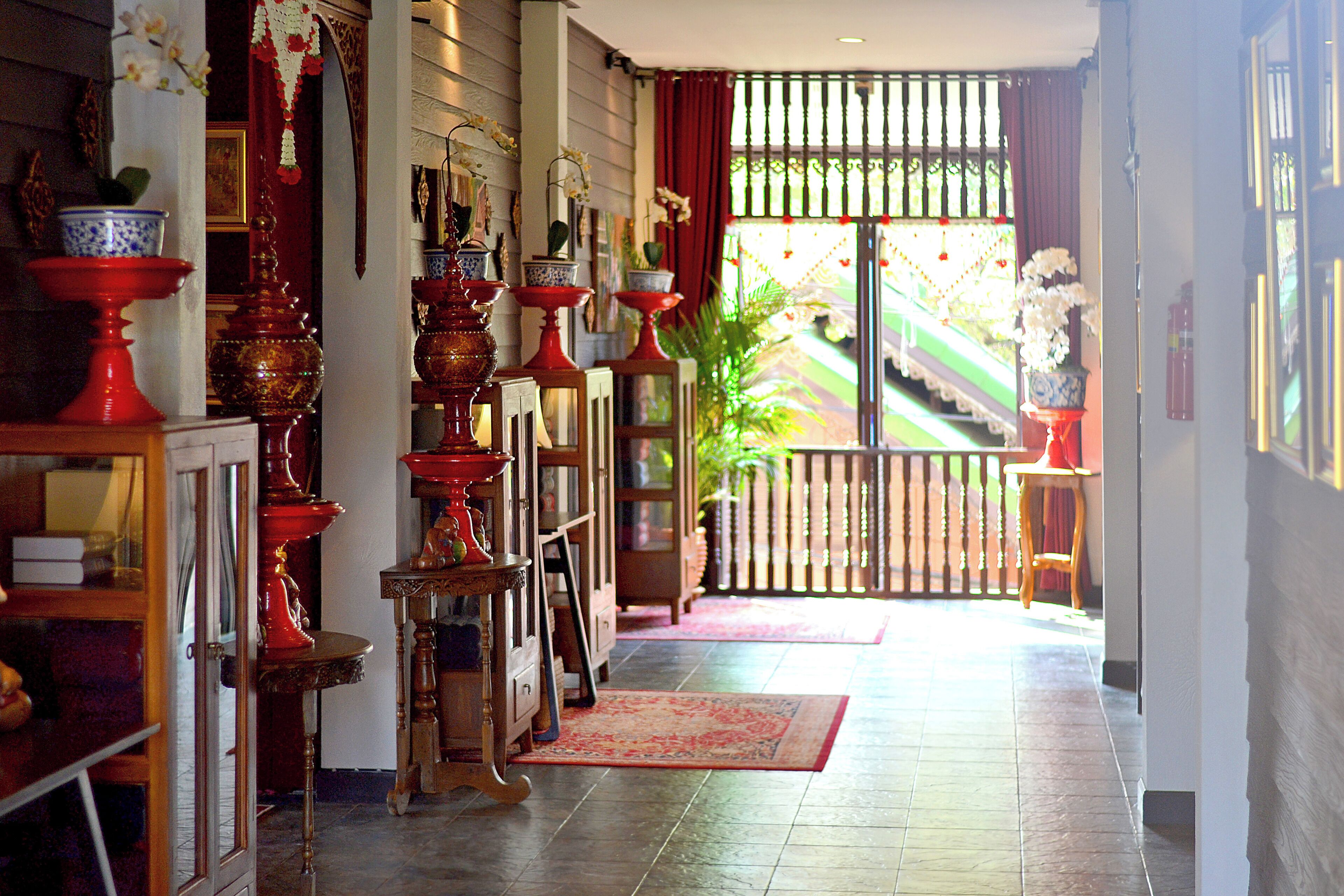 A traditional interior with ornate red and blue pottery, a wooden staircase, and a view of a garden.