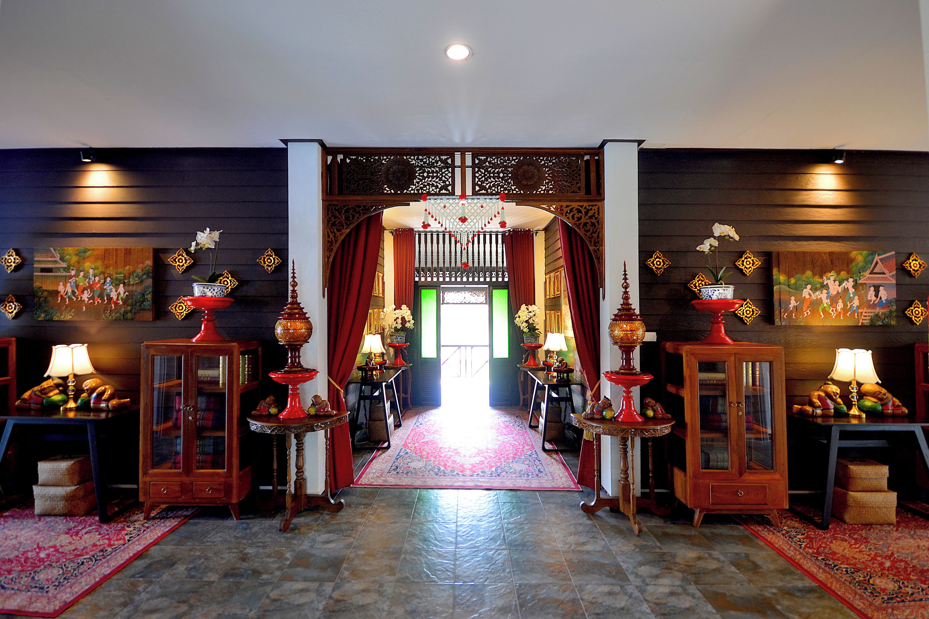 A traditional interior with a central hallway leading to a bright room, flanked by wooden cabinets and red curtains.
