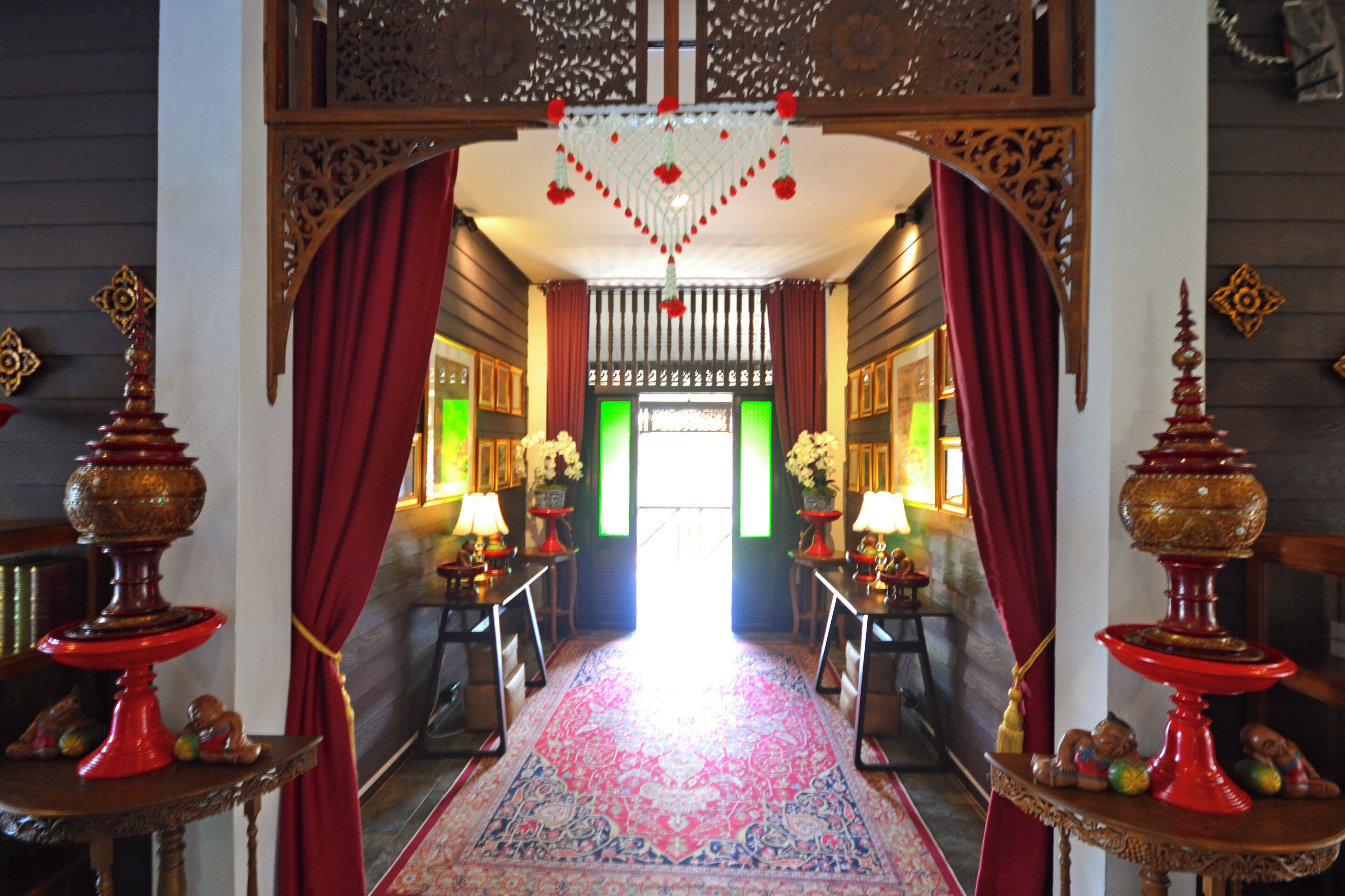 A hallway with a red carpet, ornate wooden decorations, and two red tables with decorative items.