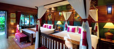 A four-poster bed with white linens and pink pillows, a red ottoman, and a wooden floor.