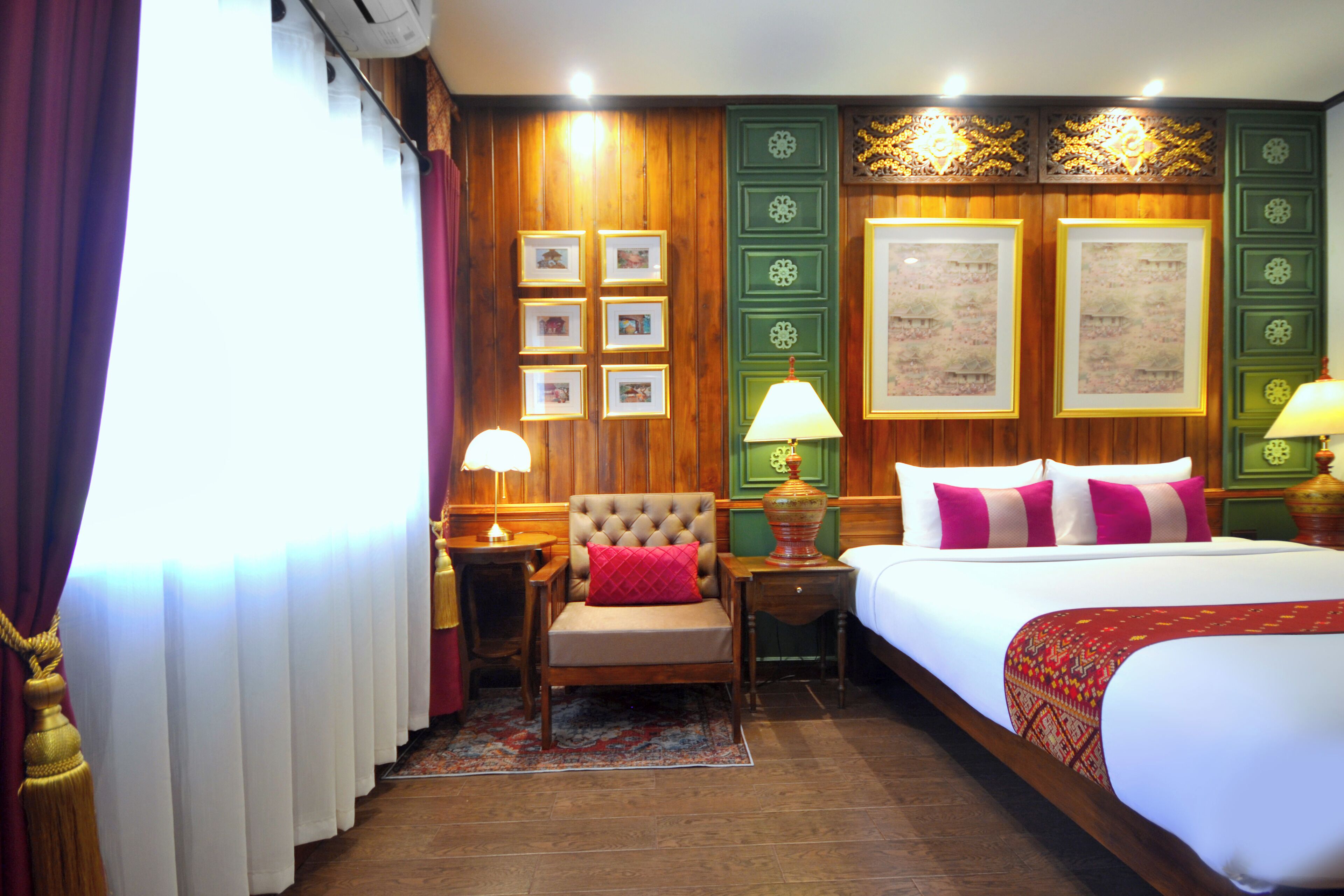 Habitación de hotel con una cama grande, una silla, una mesita de noche y una pared decorada con cuadros y una lámpara.